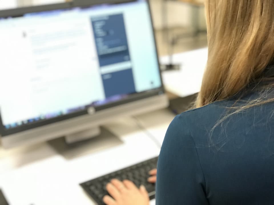 En kvinna sitter vid en datorskärm och skriver på ett tangentbord.