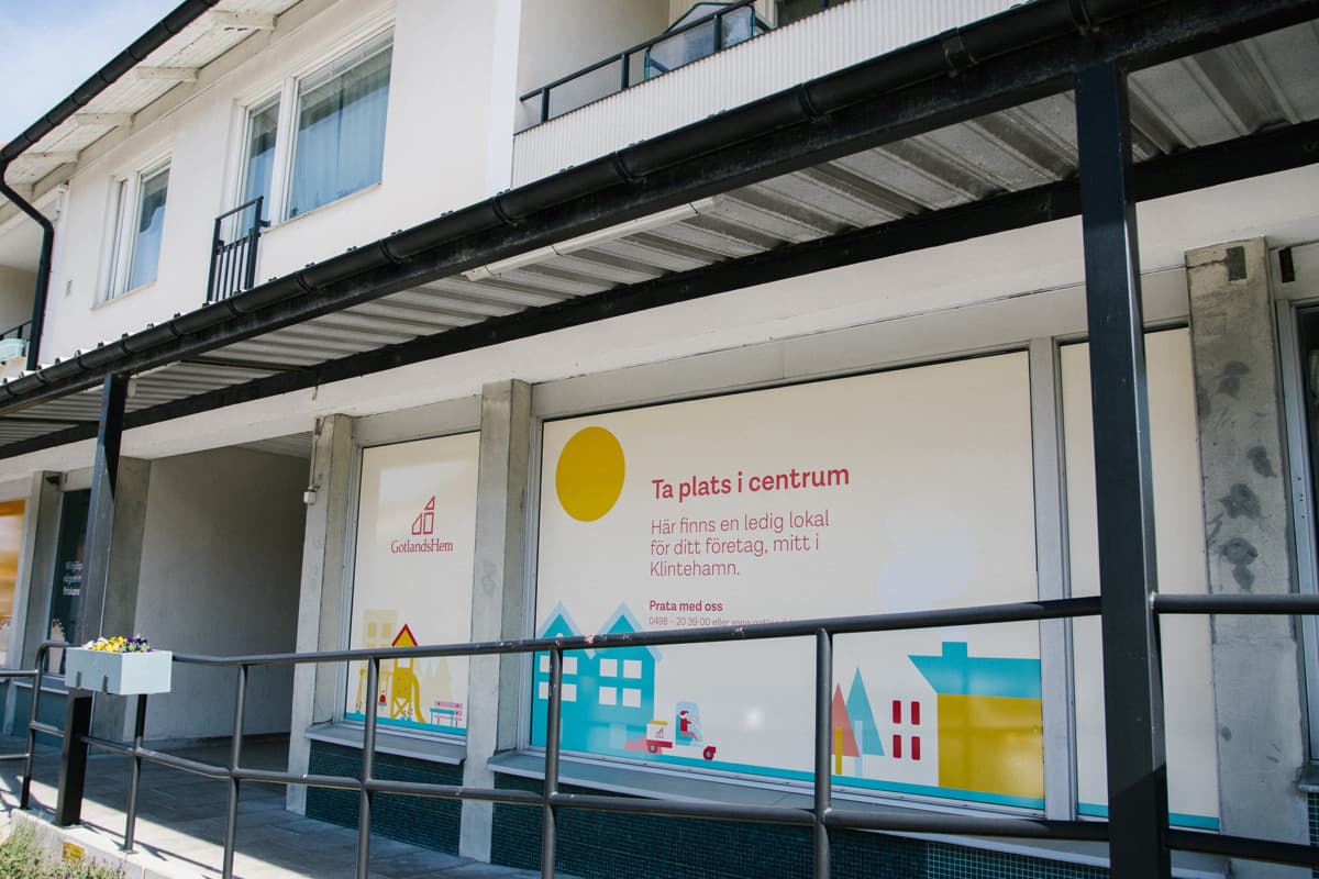 Utsidan av en byggnad med butik i bottenplan, på butiksfönstret är det uppsatt information om att hyra lokal genom GotlandsHem.