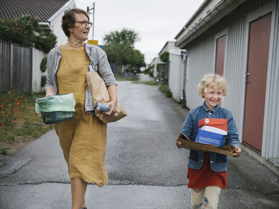 En kvinna och en flicka går med sopor i ett bostadsområde.