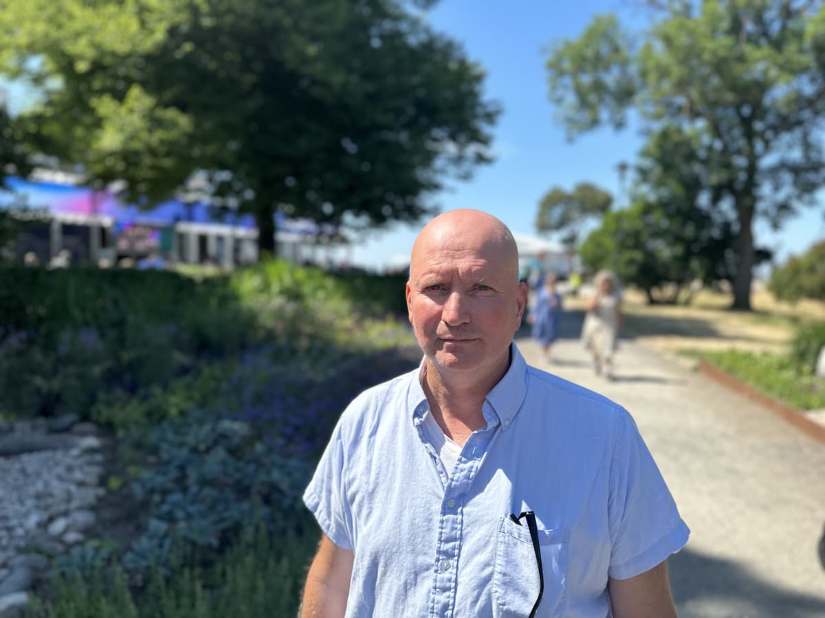 En man står i solen i en park. Han har ljusblå skjorta och tittar ini kameran.
