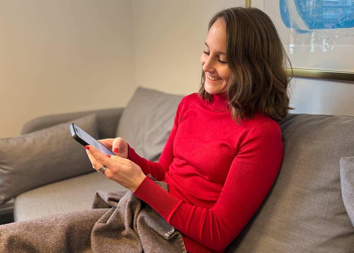 En kvinna sitter i en soffa och håller i en mobiltelefon.